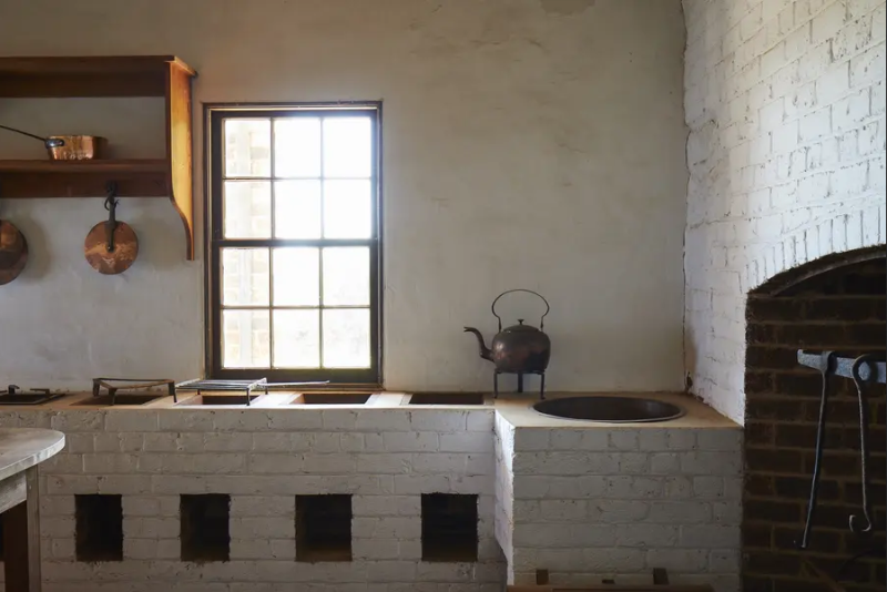 Monticello's replica stew stoves with hearth on right and kettle on counter as well as copper pans hanging